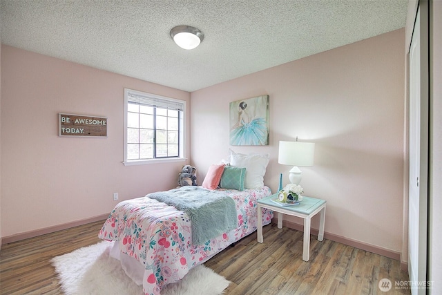 bedroom featuring baseboards, a textured ceiling, and wood finished floors