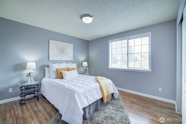 bedroom with a textured ceiling, baseboards, and wood finished floors