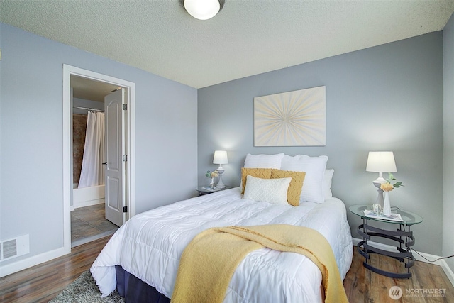 bedroom with baseboards, ensuite bath, wood finished floors, and visible vents