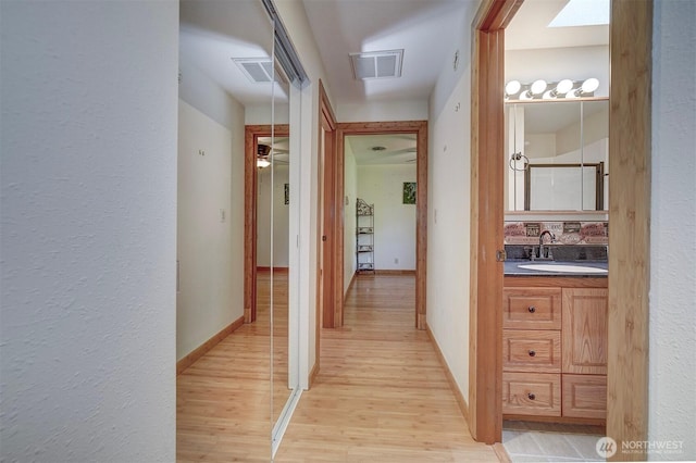 corridor with baseboards, a sink, visible vents, and light wood-style flooring