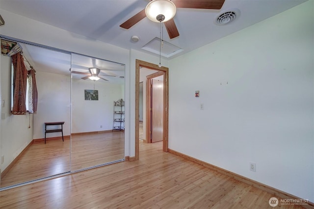 empty room featuring attic access, ceiling fan, light wood-style floors, and visible vents