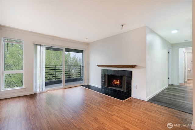unfurnished living room featuring baseboards, plenty of natural light, a tile fireplace, and wood finished floors