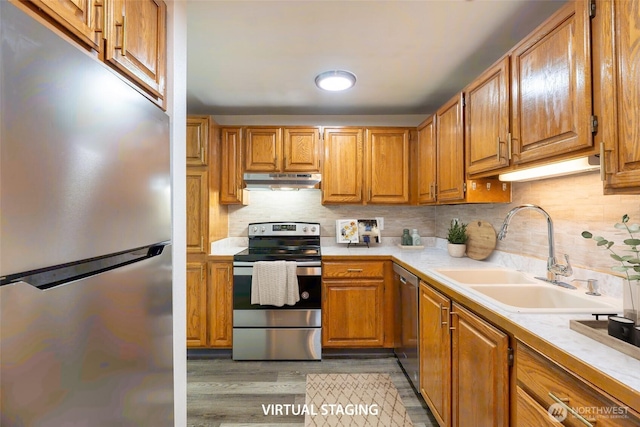 kitchen with appliances with stainless steel finishes, a sink, light wood-style floors, light countertops, and under cabinet range hood
