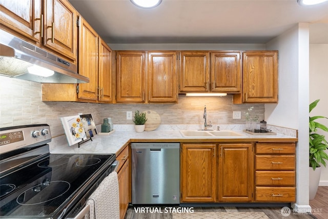 kitchen with appliances with stainless steel finishes, tasteful backsplash, a sink, light countertops, and under cabinet range hood