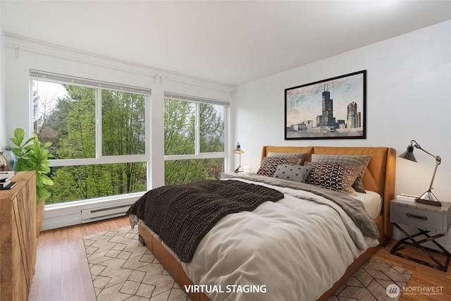 bedroom featuring multiple windows, a baseboard heating unit, and light wood-type flooring