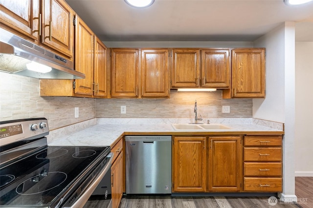 kitchen featuring brown cabinetry, dark wood-style floors, under cabinet range hood, a sink, and stainless steel appliances