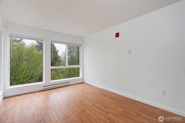 spare room featuring baseboards, a baseboard heating unit, and wood finished floors