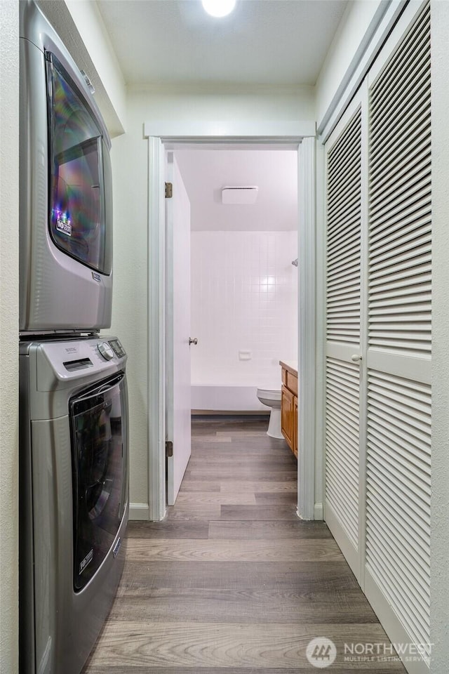 laundry area with stacked washing maching and dryer, baseboards, laundry area, and wood finished floors
