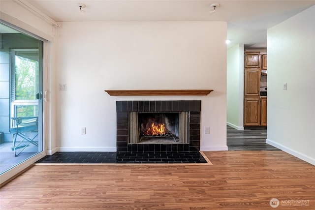 unfurnished living room featuring a fireplace with flush hearth, baseboards, and wood finished floors