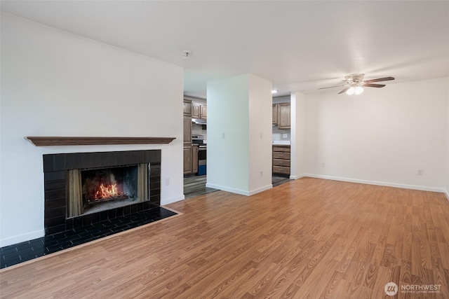 unfurnished living room featuring baseboards, a ceiling fan, light wood finished floors, and a tile fireplace