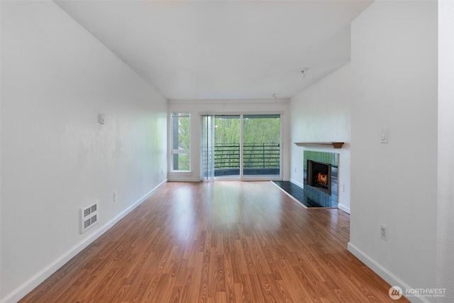unfurnished living room with baseboards, visible vents, wood finished floors, and a tile fireplace