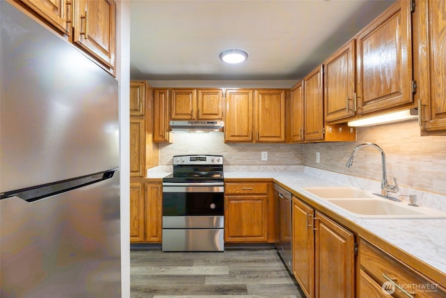 kitchen with appliances with stainless steel finishes, light wood-type flooring, a sink, light countertops, and under cabinet range hood
