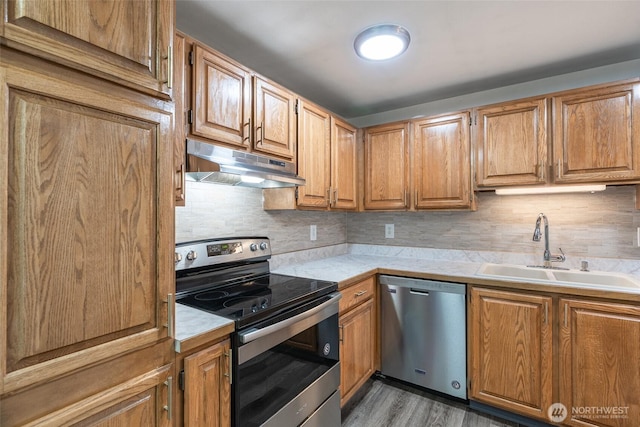 kitchen with light countertops, under cabinet range hood, a sink, appliances with stainless steel finishes, and backsplash