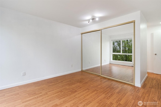 unfurnished bedroom featuring baseboards, light wood-style flooring, and a closet