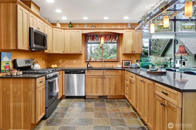 kitchen with light brown cabinets, a peninsula, appliances with stainless steel finishes, and stone finish flooring