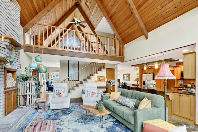 living area featuring beamed ceiling, a ceiling fan, stairs, wooden ceiling, and high vaulted ceiling