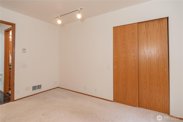 unfurnished bedroom with baseboards, track lighting, visible vents, and carpet flooring
