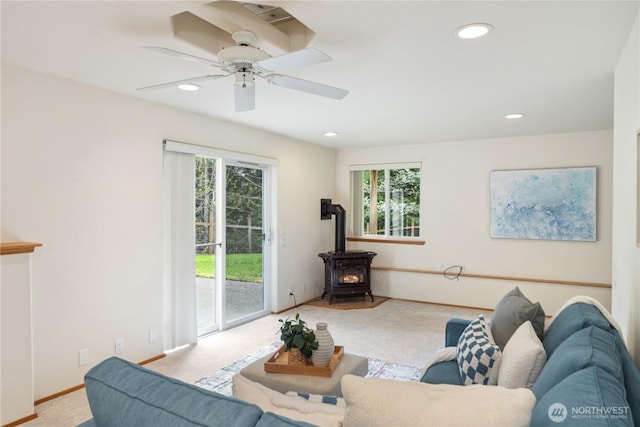 living room featuring ceiling fan, a wealth of natural light, a wood stove, and carpet