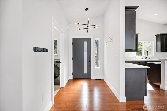 entryway with a notable chandelier, light wood finished floors, washer / clothes dryer, baseboards, and lofted ceiling
