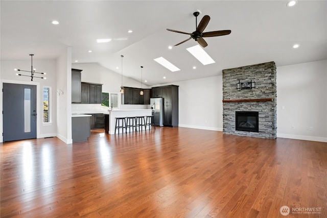 unfurnished living room with a skylight, ceiling fan, a fireplace, and dark wood-type flooring
