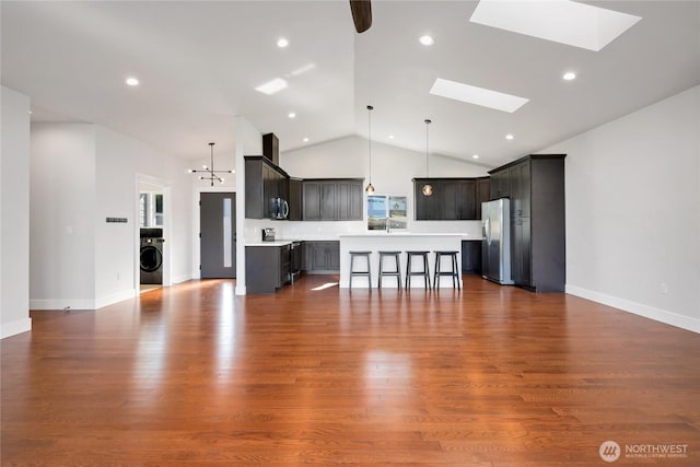 unfurnished living room featuring a skylight, baseboards, high vaulted ceiling, washer / dryer, and dark wood-type flooring