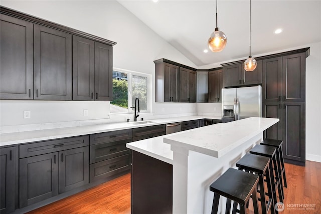 kitchen with a breakfast bar, a sink, vaulted ceiling, decorative light fixtures, and stainless steel appliances