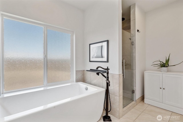 bathroom with tile patterned floors, a freestanding tub, a stall shower, and a wealth of natural light