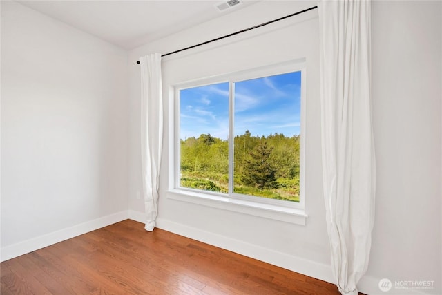 unfurnished room with baseboards, wood finished floors, and visible vents