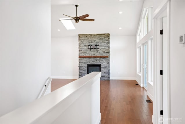hallway featuring high vaulted ceiling, visible vents, a skylight, and wood finished floors