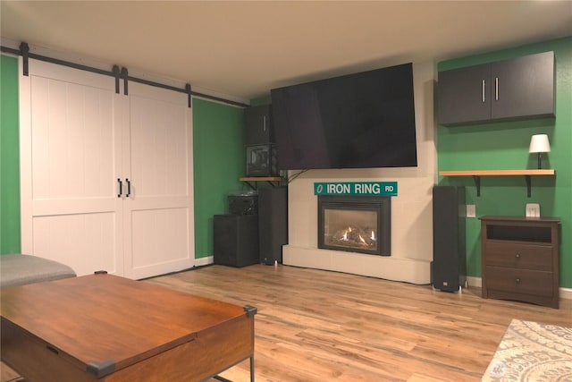 living room with baseboards, light wood finished floors, a barn door, and a warm lit fireplace