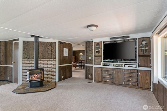 unfurnished living room with a wood stove, wooden walls, and carpet floors
