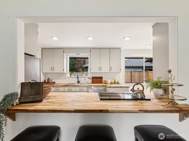kitchen with butcher block countertops, a sink, black electric cooktop, dishwasher, and recessed lighting