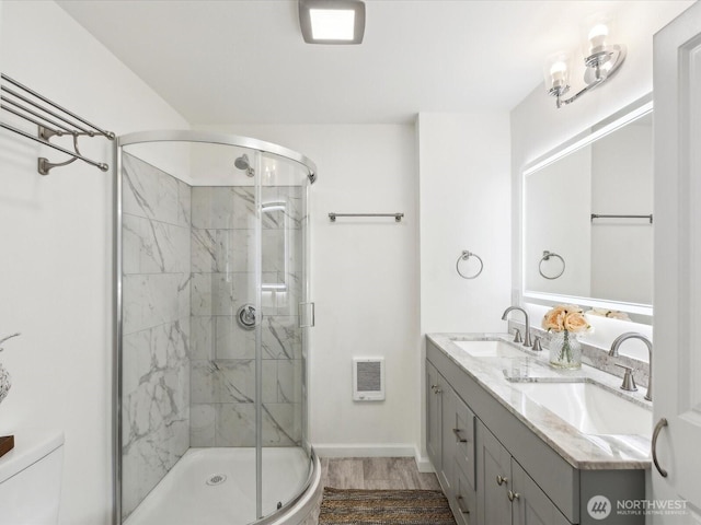 bathroom with a stall shower, toilet, wood finished floors, double vanity, and baseboards