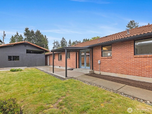 back of property with a lawn, a patio, a tiled roof, brick siding, and french doors