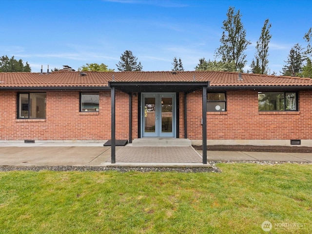 back of property with a lawn, a tiled roof, french doors, and brick siding