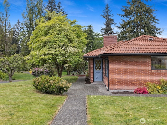 view of front of home with a tile roof, a front yard, a chimney, and brick siding