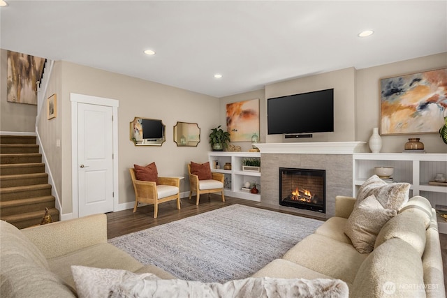 living room with a tiled fireplace, recessed lighting, stairs, and wood finished floors
