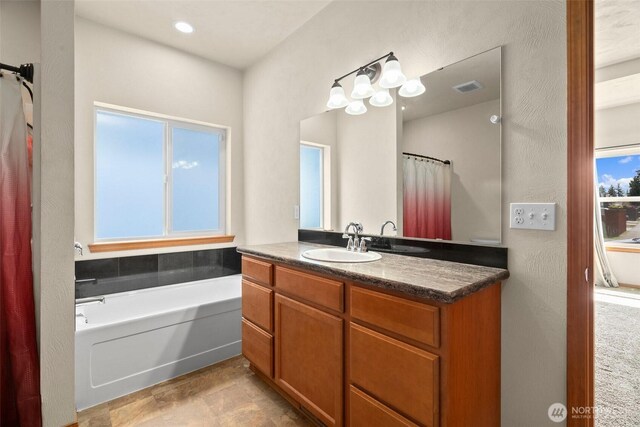 bathroom featuring a bath, vanity, visible vents, and plenty of natural light