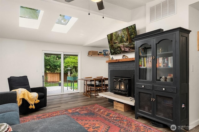 living room with wood finished floors, visible vents, a ceiling fan, lofted ceiling with skylight, and a fireplace