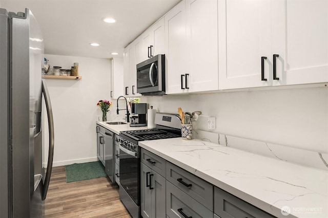 kitchen with white cabinets, a sink, baseboards, light wood-style flooring, and appliances with stainless steel finishes