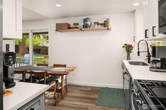 kitchen with dark wood finished floors, light stone counters, a sink, range with gas stovetop, and white cabinetry