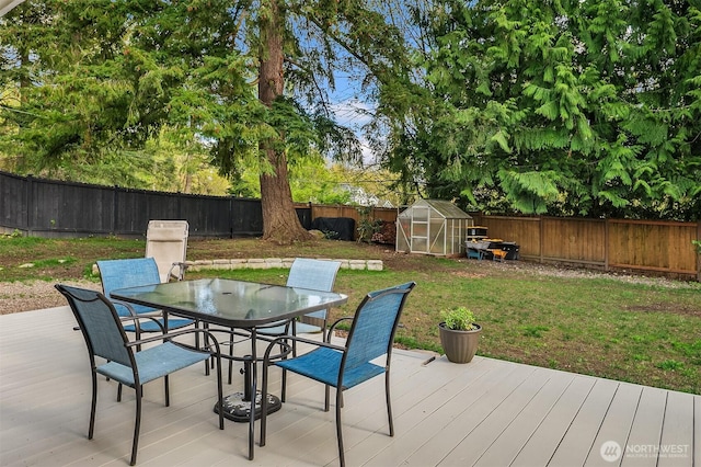 wooden deck featuring an exterior structure, a yard, outdoor dining area, and a fenced backyard