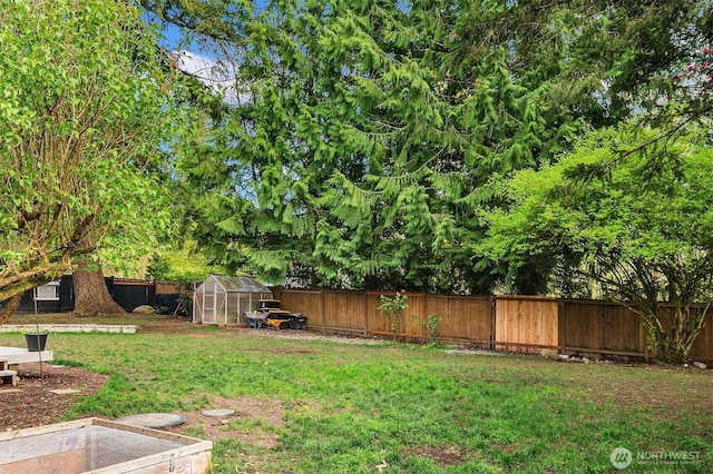 view of yard with an outdoor structure, a fenced backyard, and a greenhouse