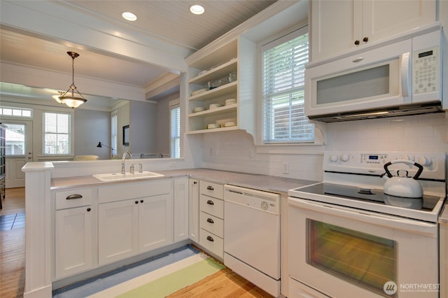 kitchen with white appliances, a sink, a peninsula, light countertops, and crown molding