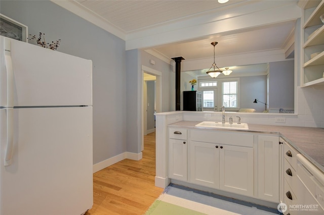 kitchen featuring freestanding refrigerator, a sink, crown molding, white cabinets, and light wood-style floors