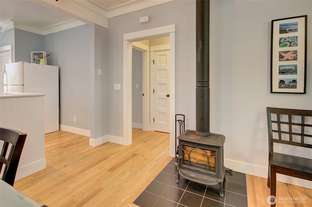 living room featuring crown molding, a wood stove, baseboards, and wood finished floors