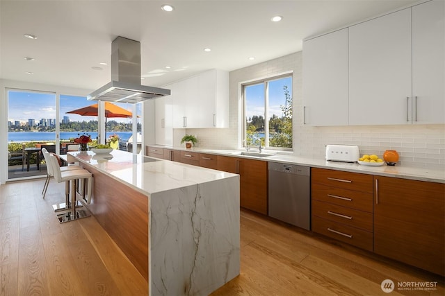 kitchen featuring a sink, light stone countertops, dishwasher, island exhaust hood, and modern cabinets