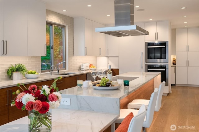 kitchen with a sink, a breakfast bar area, modern cabinets, and island range hood