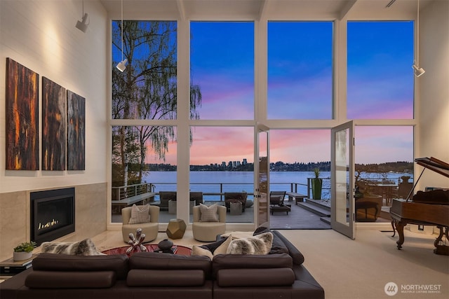 living area with a wall of windows, a towering ceiling, a lit fireplace, and a water view