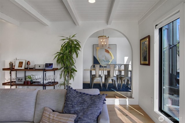 sitting room with beam ceiling, wood finished floors, a chandelier, and arched walkways